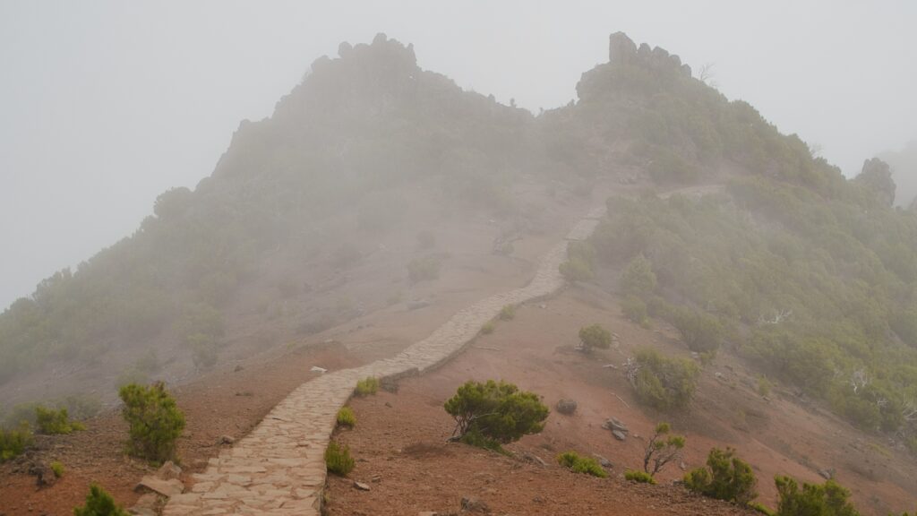 Gipfel eines Berges mit rotem Weg, der in einen Nebel führt.