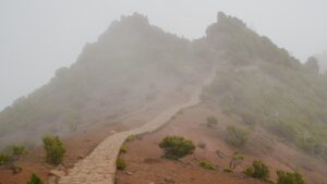 Gipfel eines Berges mit rotem Weg, der in einen Nebel führt.